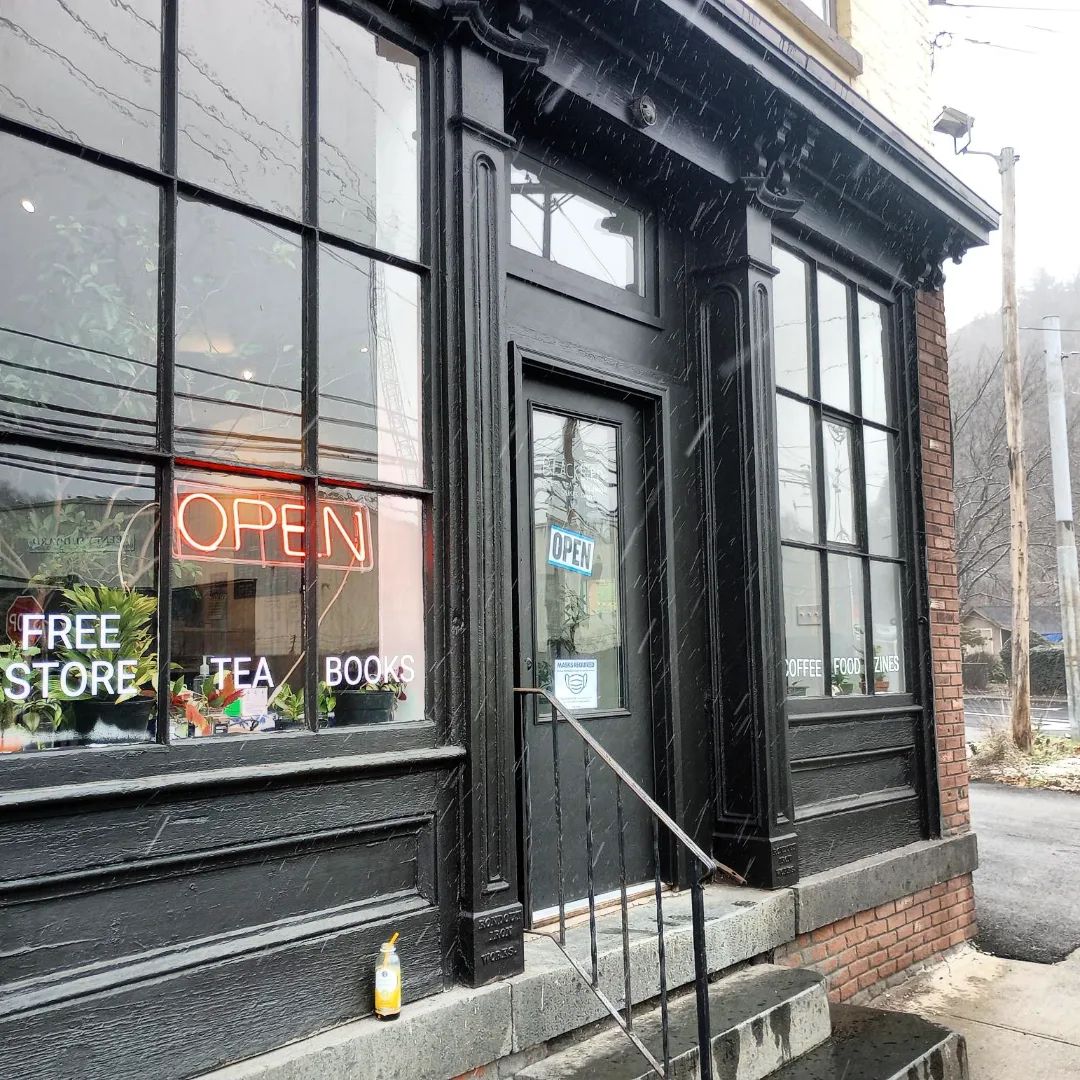 Image of the storefront at Blackbird Infoshop, door and pillars painted black, with a red neon "Open" sign in the window.